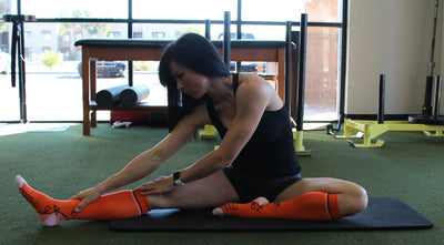 Woman doing leg stretching exercises using compression socks for women.